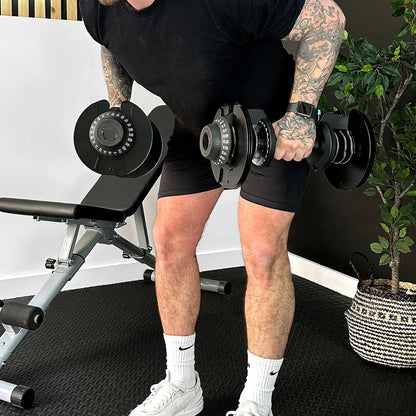 Man performing push-ups with adjustable dumbbells on a gym floor.