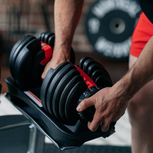 Person adjusting a set of adjustable dumbbells in a gym setting
