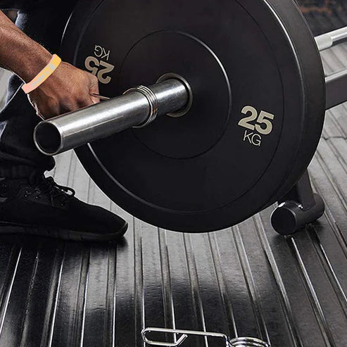 Person holding a barbell with 25 kg weight plates on a gym floor.