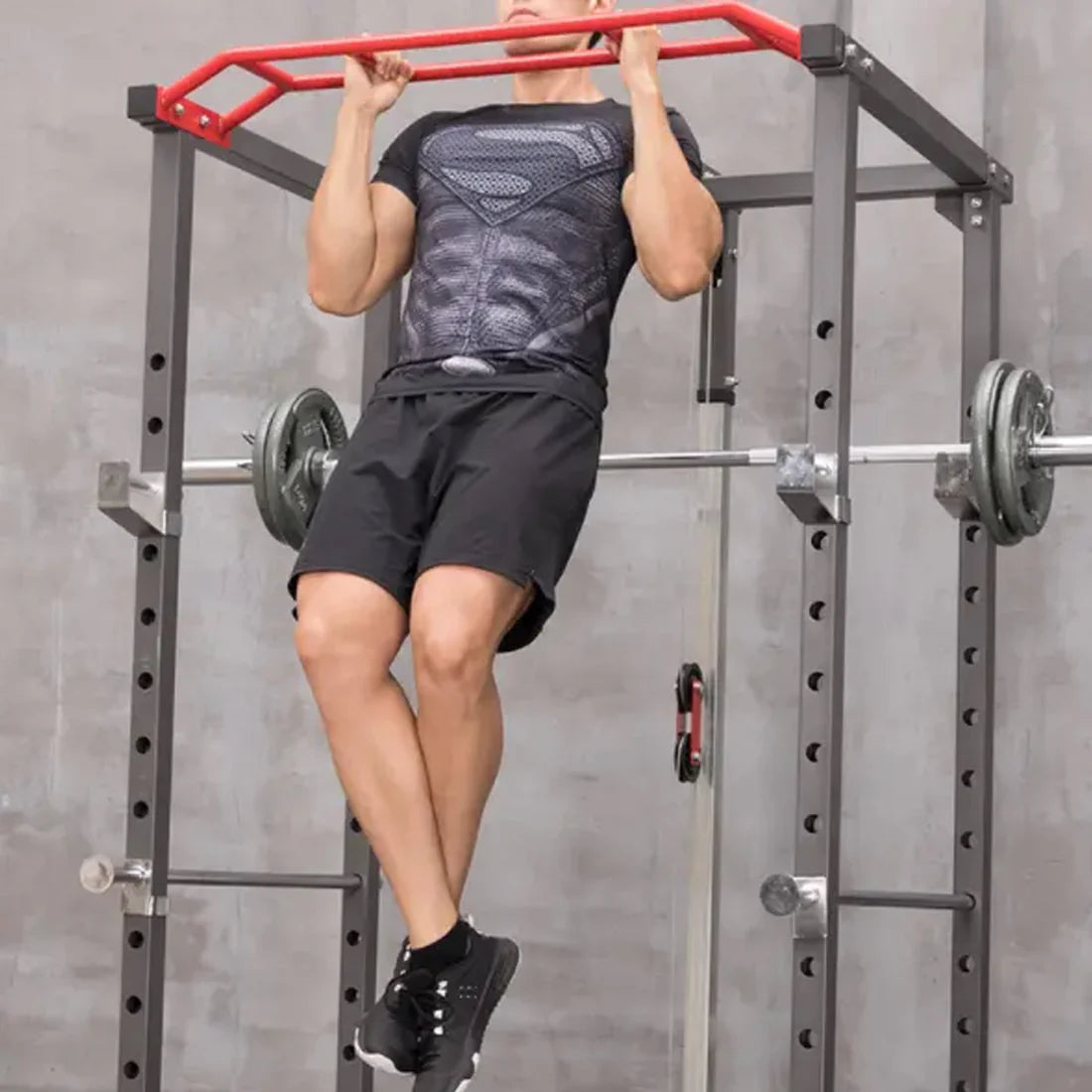 Person doing pull-ups on a red bar attached to a weight rack.